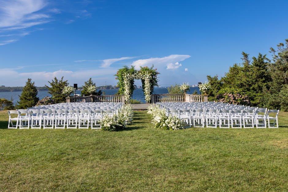 Beautiful outdoor wedding setup by the water with white chairs and floral arch in Newport, RI.